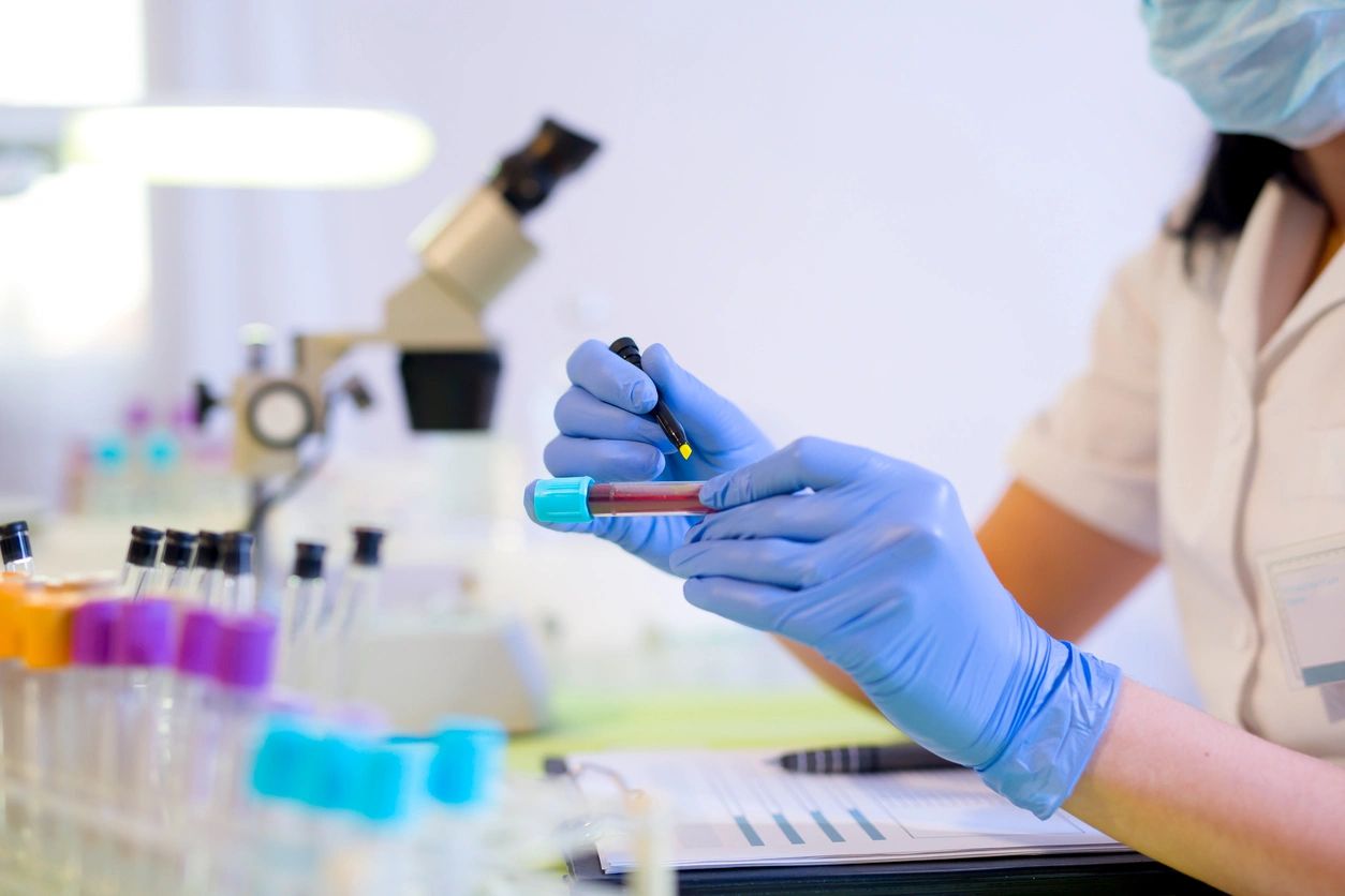 A person in blue gloves holding a tube of blood.